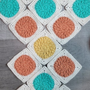 May include: A collection of 12 crocheted squares with different colored circles in the center. The squares are white with a yellow, orange, or turquoise circle in the center.