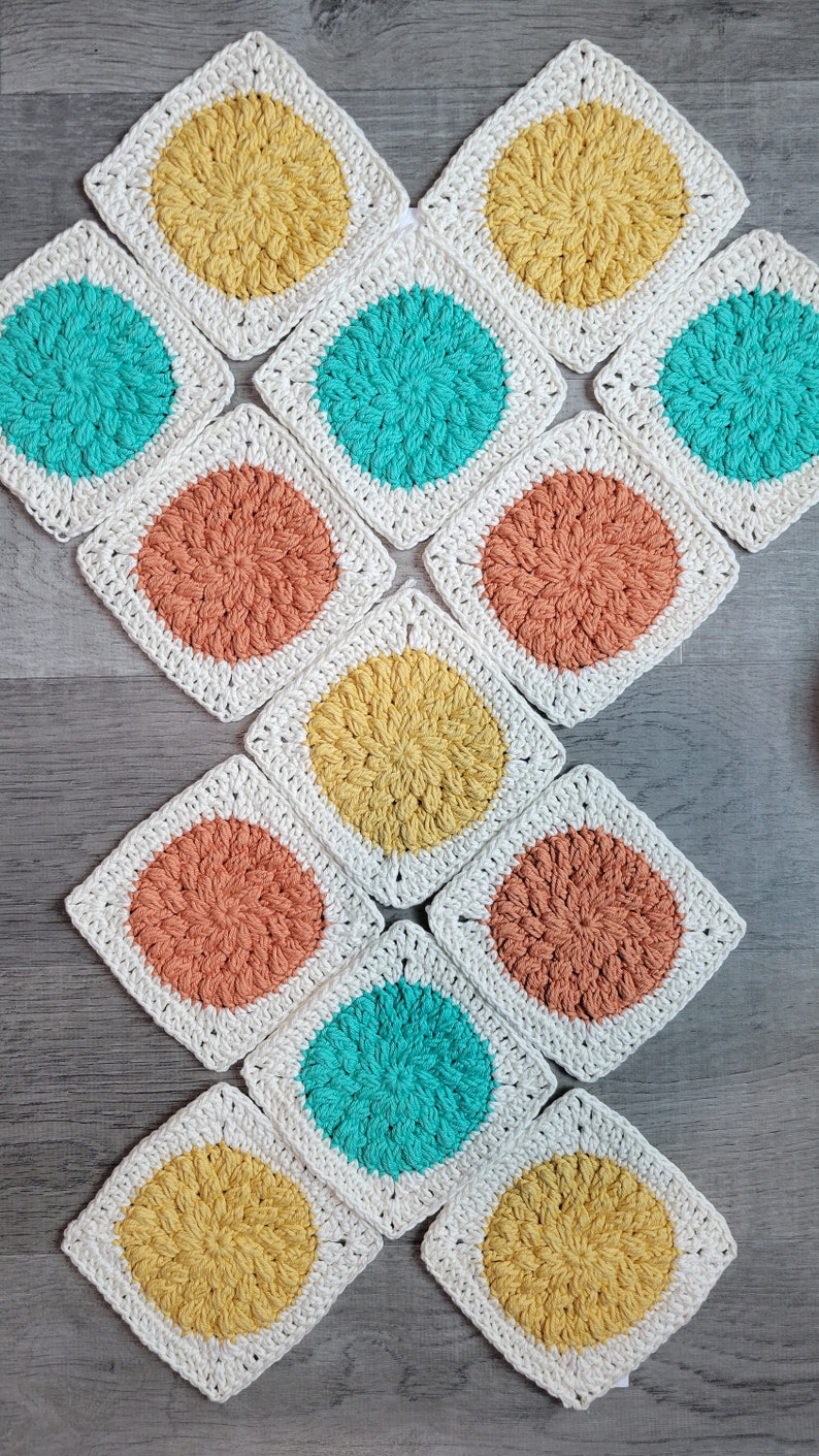 May include: A collection of 12 crocheted squares with different colored circles in the center. The squares are white with a yellow, orange, or turquoise circle in the center.