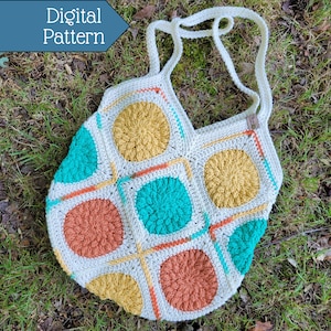 May include: A crocheted tote bag with a geometric pattern of squares and circles in shades of teal, orange, and yellow. The bag has a white background and a long strap.