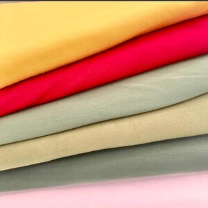 May include: A stack of colorful fabric samples in shades of yellow, red, green, and pink. The fabric appears to be a smooth, woven material, possibly cotton or linen, with a slight sheen. The layers are neatly arranged, showcasing the different colors.