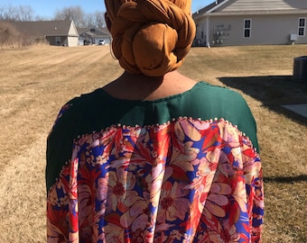 May include: A person wearing a brown turban and a colorful floral patterned dress.