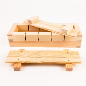 Op de afbeelding: Een houten sushi-rijstvorm met een deksel en een aparte houten pers. De vorm heeft negen compartimenten voor het maken van sushi-rollen.