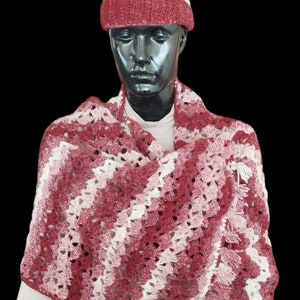 Puede incluir: Un chal de ganchillo con un patrón de degradado rosa y blanco y un gorro de ganchillo a juego con un pompón en la parte superior.