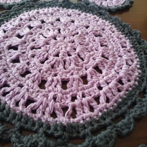 Peut inclure: Un dessous de plat en crochet violet avec une bordure en crochet gris. Le dessous de plat a un design circulaire avec un point central.