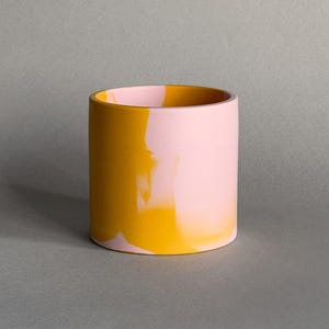 Op de afbeelding: Een gele en roze swirl keramische plantenpot. De pot is cilindrisch en heeft een gladde, glanzende afwerking.