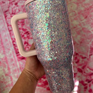 Puede incluir: Vaso cubierto de purpurina con asa y tapa. El vaso est&aacute; cubierto de purpurina iridiscente, con un asa y tapa de color rosa claro. Dise&ntilde;ado para contener bebidas.