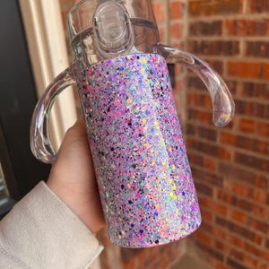 Puede incluir: Una taza para beber transparente con tapa y asas transparentes. La taza est&aacute; cubierta con un dise&ntilde;o brillante con tonos de morado, rosa y motas iridiscentes. La taza est&aacute; dise&ntilde;ada para un agarre y una bebida f&aacute;ciles.