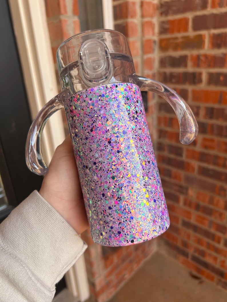 Puede incluir: Una taza para beber transparente con tapa y asas transparentes. La taza est&aacute; cubierta con un dise&ntilde;o brillante con tonos de morado, rosa y motas iridiscentes. La taza est&aacute; dise&ntilde;ada para un agarre y una bebida f&aacute;ciles.