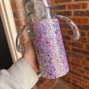 Puede incluir: Un vaso para sorber transparente con un dise&ntilde;o brillante en morado, rosa y azul. El vaso tiene una tapa transparente con cierre abatible y dos asas transparentes. El vaso est&aacute; dise&ntilde;ado para ni&ntilde;os peque&ntilde;os y ni&ntilde;os peque&ntilde;os.