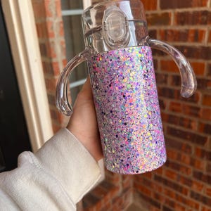 Puede incluir: Una taza para sorber transparente con un dise&ntilde;o brillante p&uacute;rpura e iridiscente. La taza tiene dos asas transparentes y una tapa transparente con cierre abatible. La taza est&aacute; dise&ntilde;ada para ni&ntilde;os peque&ntilde;os y ni&ntilde;os peque&ntilde;os.