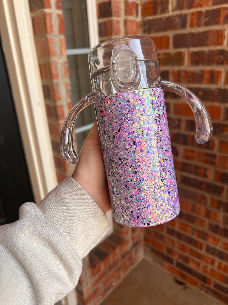 Puede incluir: Una taza para sorber transparente con un dise&ntilde;o brillante p&uacute;rpura e iridiscente. La taza tiene dos asas transparentes y una tapa transparente con cierre abatible. La taza est&aacute; dise&ntilde;ada para ni&ntilde;os peque&ntilde;os y ni&ntilde;os peque&ntilde;os.