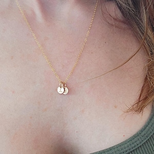May include: A gold-coloured necklace with a delicate chain. The necklace features two small, round pendants, each with a single initial. The pendants are suspended from the chain, creating a simple and elegant design.