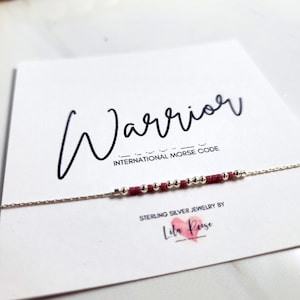 Peut inclure: Un bracelet en argent avec un motif en code Morse. Le bracelet comporte de petites perles rondes argentées et des perles bordeaux épelant le mot "Warrior". Le bracelet est présenté sur une carte blanche avec le mot "Warrior" écrit en cursive.