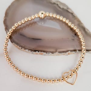 Peut inclure: Bracelet doré composé de petites perles rondes et d'un charm en forme de cœur. Un gros bouton doré est placé au sommet du bracelet. Le charm en forme de cœur est délicat.