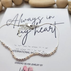 Peut inclure: Un bracelet délicat en argent sterling avec une série de petites perles argentées et des perles rose clair. Le bracelet est sur une carte blanche avec les mots "Always in my heart" et "STERLING SILVER JEWELRY BY Lila Rose".