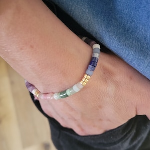 May include: A multi-coloured gemstone bracelet featuring pink, green, blue, and purple beads, interspersed with gold-coloured spacers. The bracelet is made of small, round beads strung together. The bracelet is worn on a wrist. The gemstones are measured in millimetres.