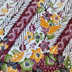 Pode incluir: Um tecido branco com um padrão repetitivo de desenhos florais de cor bordô, amarelo e verde. O padrão é um desenho batik tradicional.