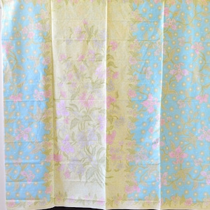 Op de afbeelding: Een paneel stof met een herhalend bloemenpatroon in tinten blauw, roze en geel. De stof is verdeeld in drie verticale secties, elk met een ander bloemenontwerp.