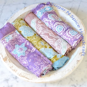 Op de afbeelding: Vier kleurrijke vierkante stoffen met bloemenpatronen zijn gevouwen en gestapeld in een witte houten kom. De kom heeft de tekst "Sugar N Spice Handcraft" aan de zijkant.