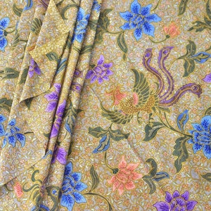 Peut inclure: Gros plan sur un tissu à fond doré avec un motif répétitif de fleurs et d'oiseaux violets, bleus et roses. Le tissu est plié de manière à créer un effet de superposition.