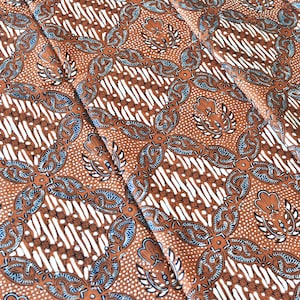 May include: Brown fabric with a repeating floral pattern. The design features stylized flowers and leaf shapes in shades of brown, white, and blue. The fabric has a textured appearance, with a detailed and intricate design.