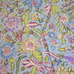Könnte beinhalten: Ein blauer Stoff mit einem floralen Muster. Das Muster zeigt rosa, gelbe und weiße Blumen mit grünen Blättern. Der Stoff hat eine subtile Textur.