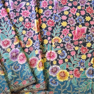Könnte beinhalten: Eine Nahaufnahme eines bunten Stoffes mit einem Blumenmuster. Der Stoff ist in mehreren Schichten gefaltet und zeigt einen blauen Hintergrund mit filigranen Details. Die Blumen sind in den Farben Rosa, Rot, Gelb und Blau gehalten, die Blätter sind grün.