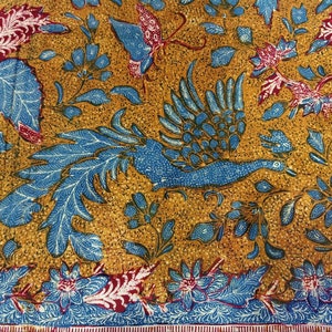 Könnte beinhalten: Nahaufnahme eines Stoffes mit einem sich wiederholenden Muster aus blauen und roten Blumen und Vögeln auf goldenem Hintergrund. Der Stoff hat ein traditionelles indonesisches Batik-Design.