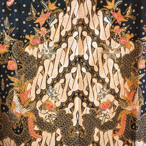 May include: A black fabric with a traditional Indonesian batik pattern. The pattern features a large central motif of stylized figures in beige and gold, surrounded by smaller floral and bird motifs. The background is a dark black with small white dots.