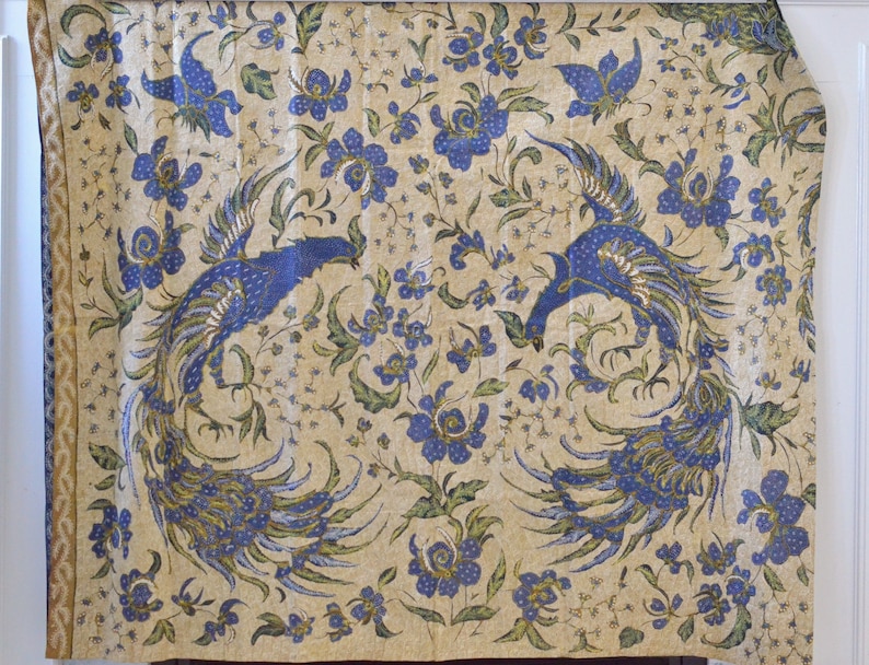 May include: A cream-colored fabric with a repeating pattern of blue and green peacocks and blue flowers. The fabric has a gold border.