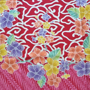 以下が含まれることがあります： 白とピンクの花柄の赤い布。花は黄色、オレンジ、紫、ピンクの色合いです。布は渦巻きと線の繰り返し模様です。