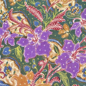 May include: A green fabric with a colorful floral pattern. The pattern features purple, red, yellow, and blue flowers with intricate details. The fabric has a textured surface.