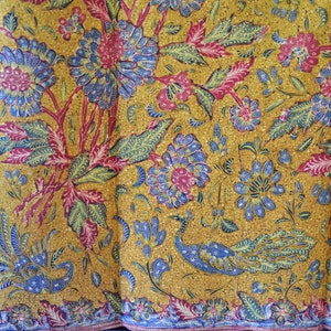 Könnte beinhalten: Ein gelber Stoff mit einem blauen und roten Blumenmuster. Der Stoff zeigt im Zentrum ein Pfauenmotiv.