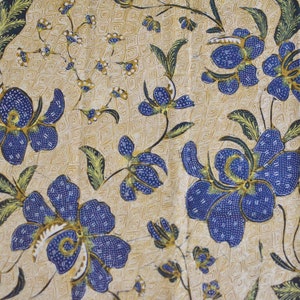 May include: A beige fabric with a repeating pattern of blue flowers with green leaves. The flowers have a small white center and are outlined in gold.