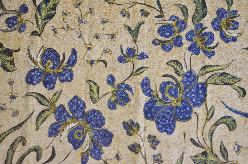 May include: A beige fabric with a repeating pattern of blue flowers with green leaves. The flowers have a small white center and are outlined in gold.