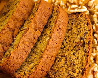 May include: Close-up of a loaf of banana bread sliced into four pieces. The bread is golden brown and has a crumbly texture. The bread is topped with walnuts.