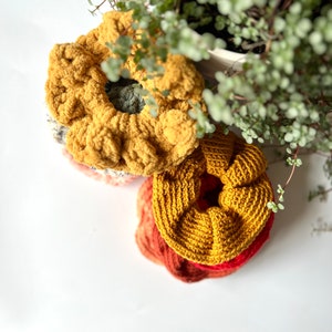 May include: Three crocheted hair scrunchies in shades of yellow, orange, and red. The scrunchies are stacked on top of each other.