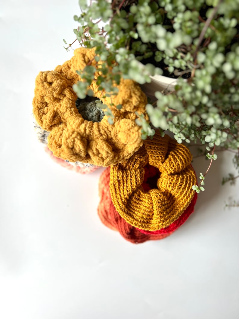 May include: Three crocheted hair scrunchies in shades of yellow, orange, and red. The scrunchies are stacked on top of each other.
