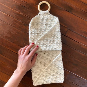 Pu&ograve; includere: Un organizzatore appeso in crochet bianco con un anello di legno in cima. L'organizzatore &egrave; piegato a met&agrave; e ha due scomparti.