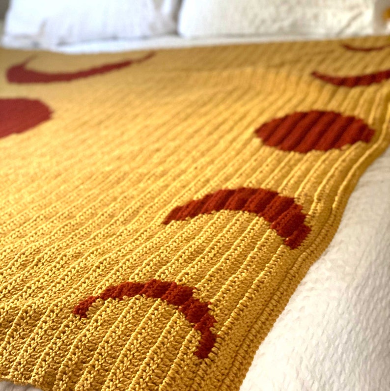 May include: A crocheted throw blanket in a mustard yellow colour with a pattern of red crescent moons.