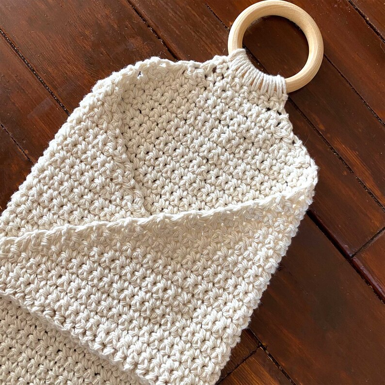 Pu&ograve; includere: Una borsa in crochet bianca con un manico ad anello in legno. La borsa &egrave; realizzata con un semplice motivo a punto e ha un aspetto naturale e rustico.