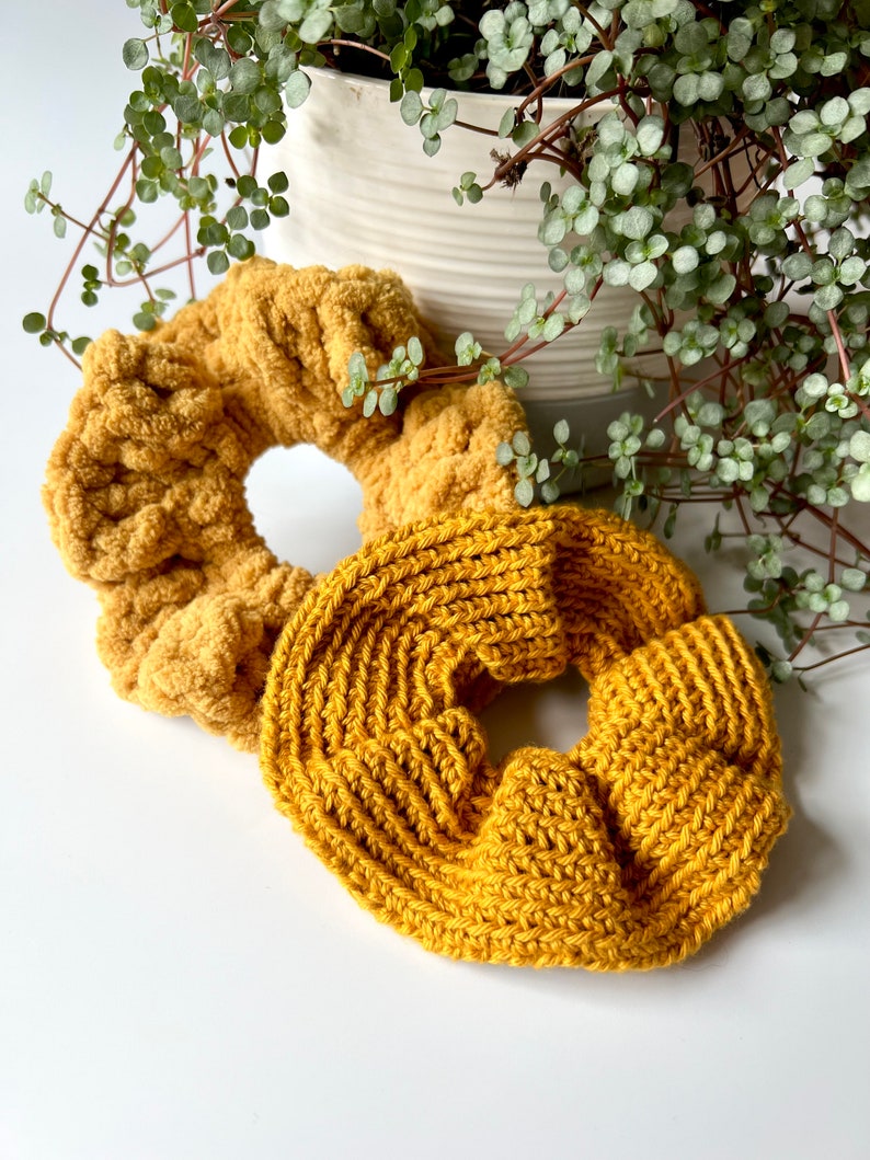 May include: Two yellow knitted hair scrunchies. One is a fluffy, textured scrunchie and the other is a smooth, ribbed scrunchie.