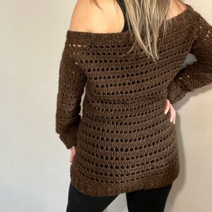 Pu&ograve; includere: Un maglione di uncinetto marrone con scollo a barca e maniche lunghe.