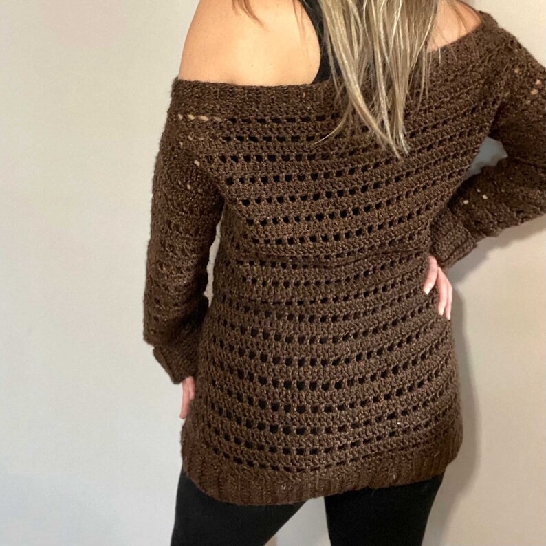 Pu&ograve; includere: Un maglione di uncinetto marrone con scollo a barca e maniche lunghe.