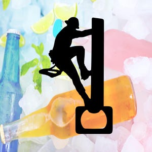 May include: Black metal bottle opener featuring a silhouette of a rock climber ascending a wall. The opener is positioned over a beer bottle, with ice, lime slices, and other bottles in the background. A fun and unique bar accessory.