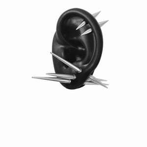May include: A black ear-shaped earring with multiple silver spikes protruding from the surface. The spikes are of varying lengths and are arranged to create a bold, edgy aesthetic. The earring is set against a white background.