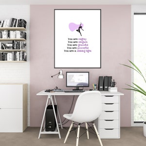 May include: A framed print with a black frame featuring a dancer silhouette and inspirational text: "You are mighty, elegant, graceful, powerful, a shining light." The print hangs above a white desk with a computer and office supplies.