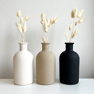 Pode incluir: Tr&ecirc;s vasos de cer&acirc;mica em branco, bege e preto com grama de pampas seca em cada um.