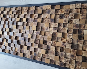 Op de afbeelding: Een rechthoekig wandkunstwerk bestaande uit talloze kleine, vierkante houten blokjes met variërende dieptes. De blokjes hebben een natuurlijke houtnerf met geblakerde, donkerbruine randen en lichtere bruine centra in een zwart frame.