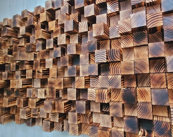 Op de afbeelding: Een wandkunstwerk bestaande uit talloze vierkante houten blokken van verschillende dieptes, wat een driedimensionaal textuuroppervlak creëert. Elk blok heeft een geblakerde, donkerbruine afwerking met zichtbare natuurlijke houtnerven.